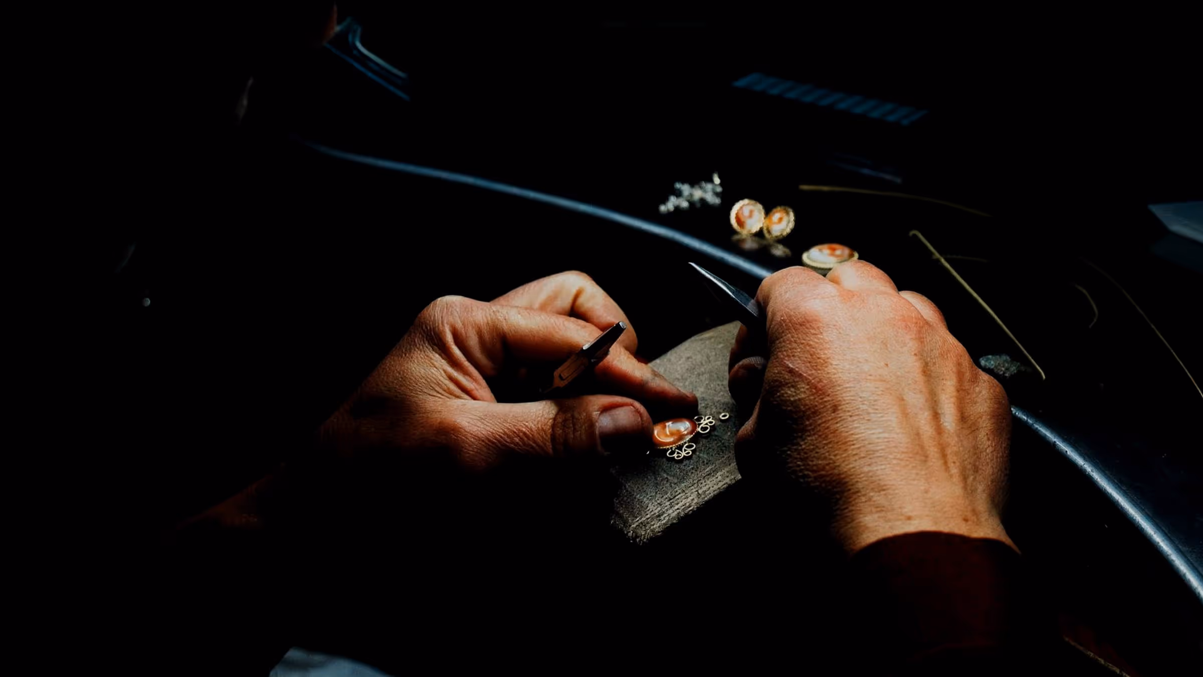 A hand at the bench under a warm lamp, filings across the pin